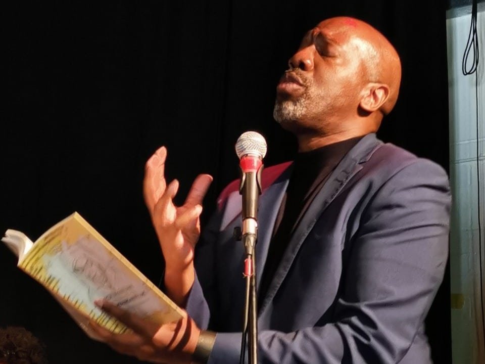 Roy McFarlane, a black, bald performance poet reads passionately